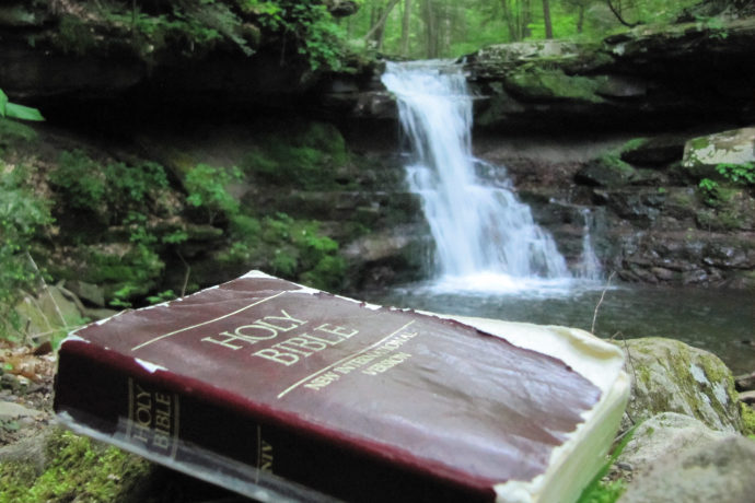 Holy Bible pictured near an outdoor waterfall.